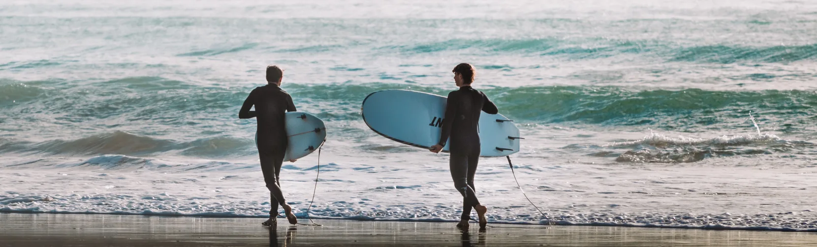 Two surfers carrying boards into the waves at Raglan Beach, one of New Zealand’s most famous surfing destinations in Waikato