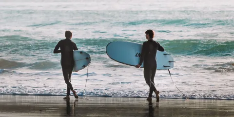 Two surfers carrying boards into the waves at Raglan Beach, one of New Zealand’s most famous surfing destinations in Waikato