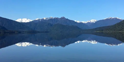 Crystal-clear reflection of snow-capped mountains and forest in Lake Kaniere near Hokitika on the West Coast of New Zealand’s South Island