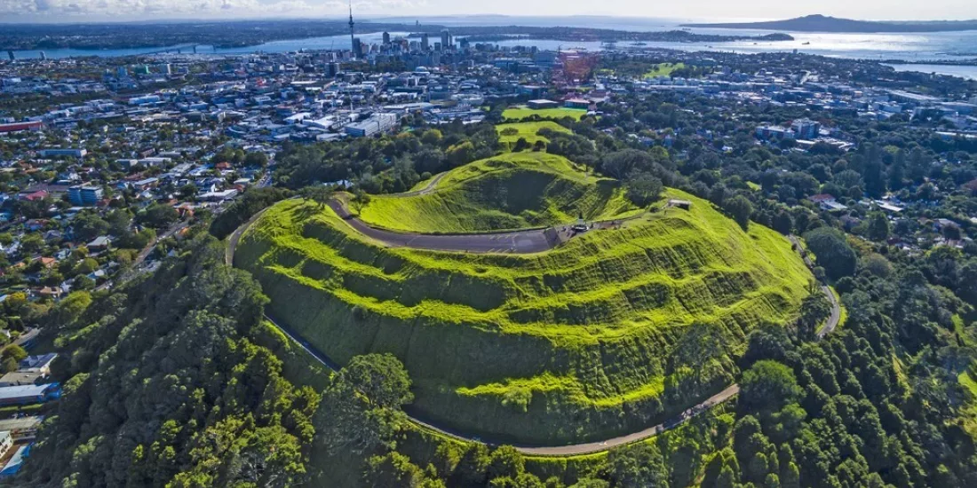 Drone aerial view of Mount Eden’s lush volcanic crater and surrounding green landscape in Auckland, New Zealand.