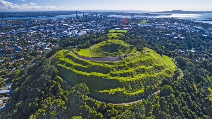 Drone aerial view of Mount Eden’s lush volcanic crater and surrounding green landscape in Auckland, New Zealand.