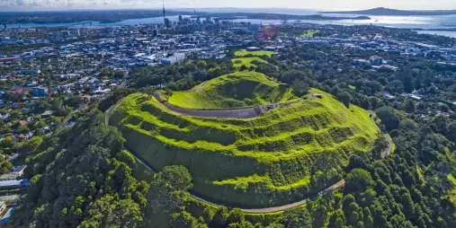 Drone aerial view of Mount Eden’s lush volcanic crater and surrounding green landscape in Auckland, New Zealand.