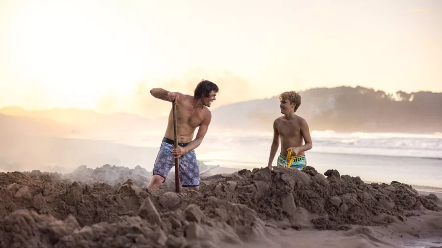 Two boys digging thermal pools at Hot Water Beach at sunset
