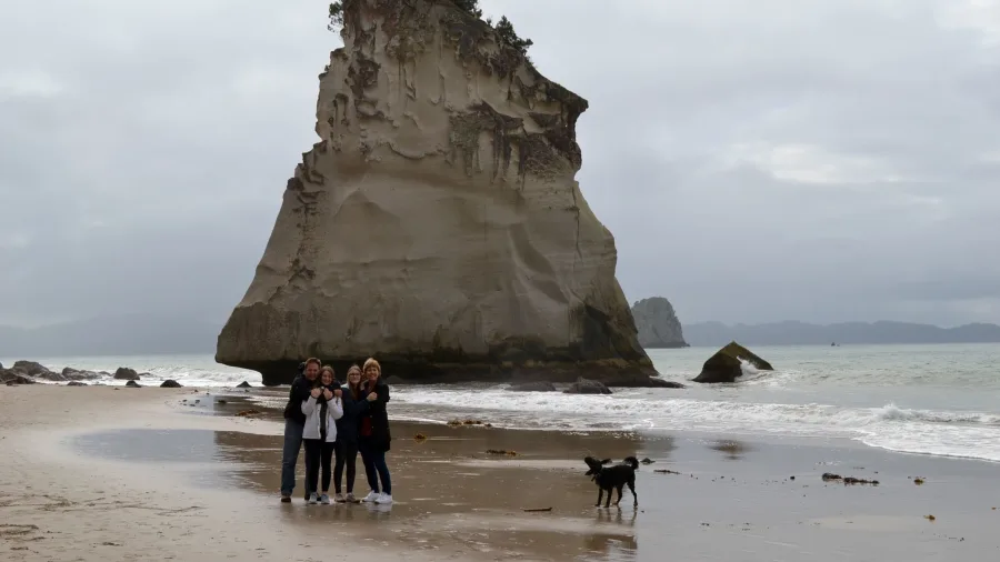 Te Hoho Rock sea stack on Cathedral Cove Beach with people and a dog in the foreground