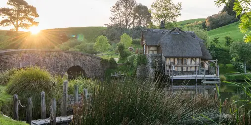 Stone bridge and The Mill at Hobbiton at sunset with lush green hills