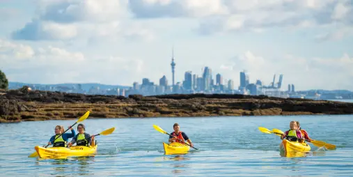 paddlers kayaking near Rangitoto Island with Auckland skyline and Sky Tower in the distance