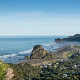 Rugged black sand shoreline at Piha Beach with Lion Rock and waves rolling in from the Tasman Sea