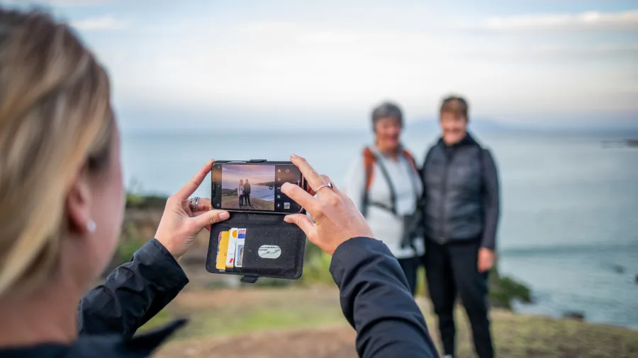 Guest taking a photo of two people standing outdoors with scenic coastal views in Matakana on the Art & Kiwi Classic Experience tour near Auckland, New Zealand.