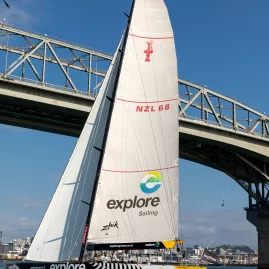 The America's Cup yacht NZL68 sailing under Auckland Harbour Bridge on a sunny day