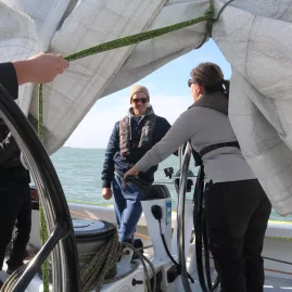 Sailing crew adjusting sails near the helm while navigating open waters