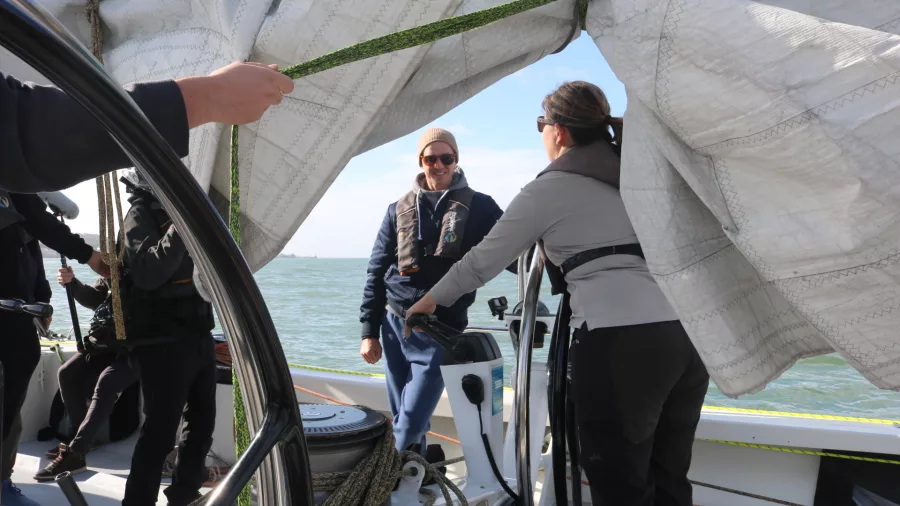 Sailing crew adjusting sails near the helm while navigating open waters