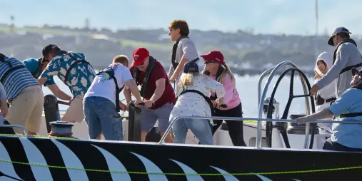 Guests working the grinders aboard an America's Cup yacht on Waitematā Harbour in Auckland