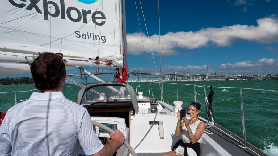 A passenger enjoying a photo opportunity on a sailing yacht in Auckland Harbour with the city and bridge in the background
