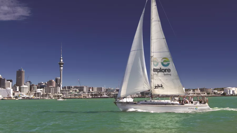 A sailing yacht gliding through Auckland Harbour with the iconic Sky Tower and city skyline in the background