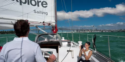 A passenger enjoying a photo opportunity on a sailing yacht in Auckland Harbour with the city and bridge in the background