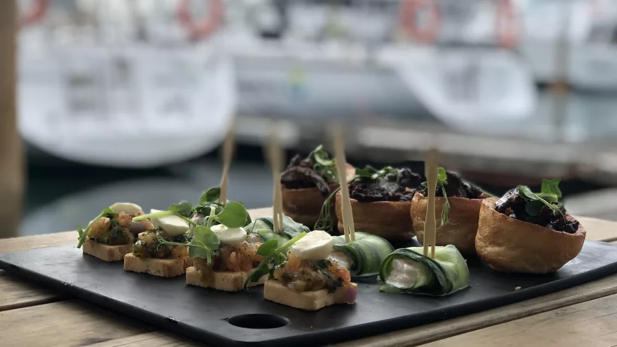A selection of gourmet appetisers elegantly presented on a black serving board, with luxury yachts docked in the background.