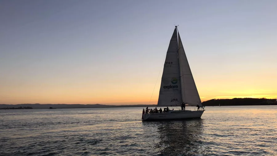 A sailing yacht gliding across calm waters at sunset, with a golden sky reflecting on the ocean.