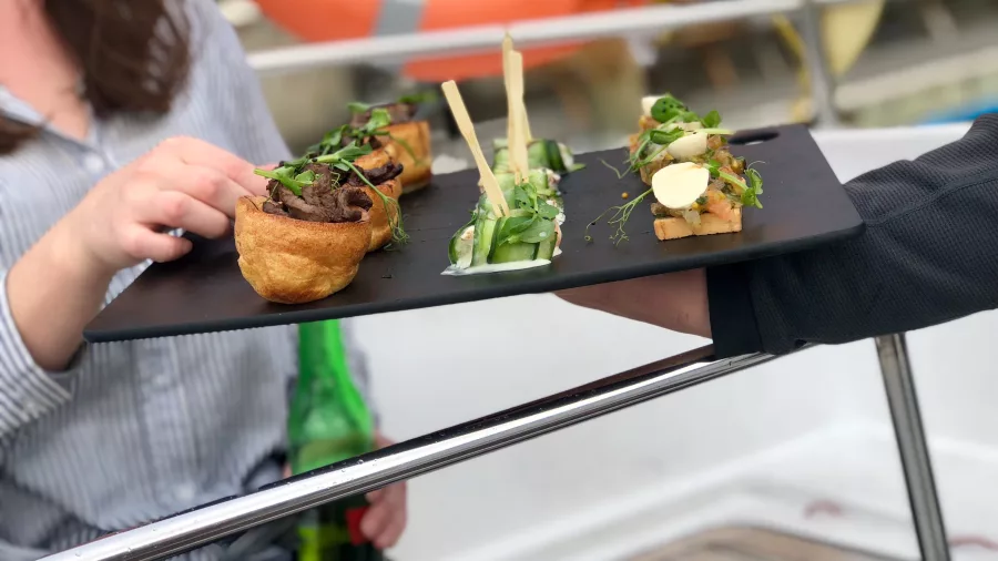 A tray of gourmet canapés being served aboard a yacht, with a guest reaching for a delicious bite.
