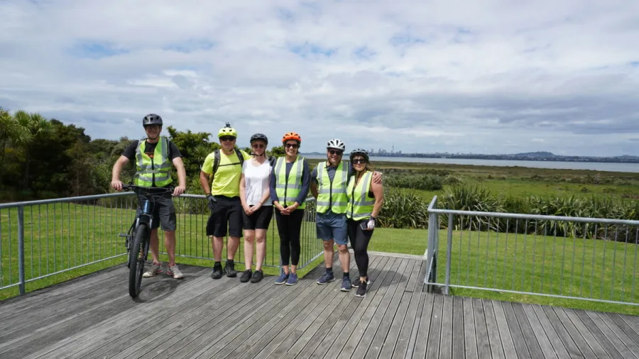 Cyclists posing for a group photo on a lookout platform with coastal views