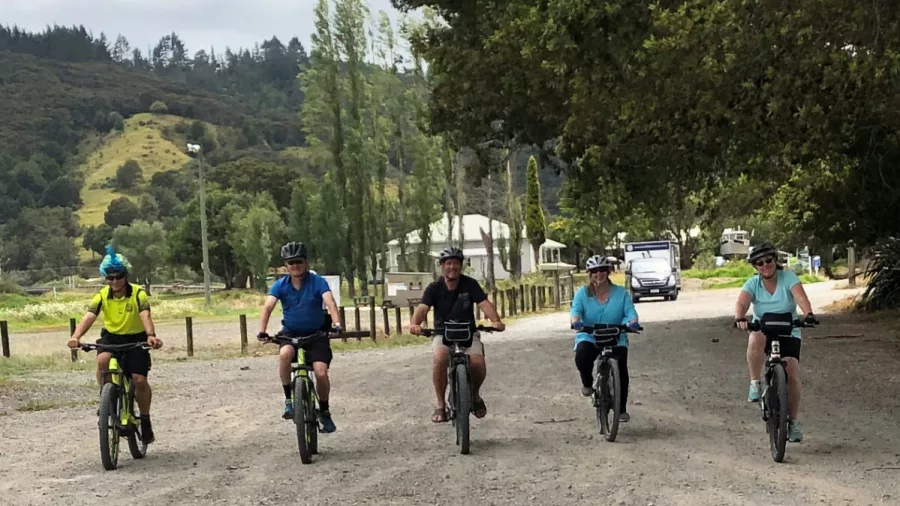 Group of cyclists riding e-bikes along a rural gravel road in Auckland