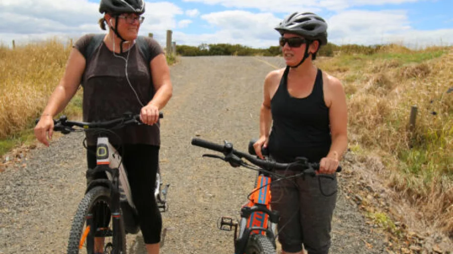Two women standing with their e-bikes chatting on a gravel trail