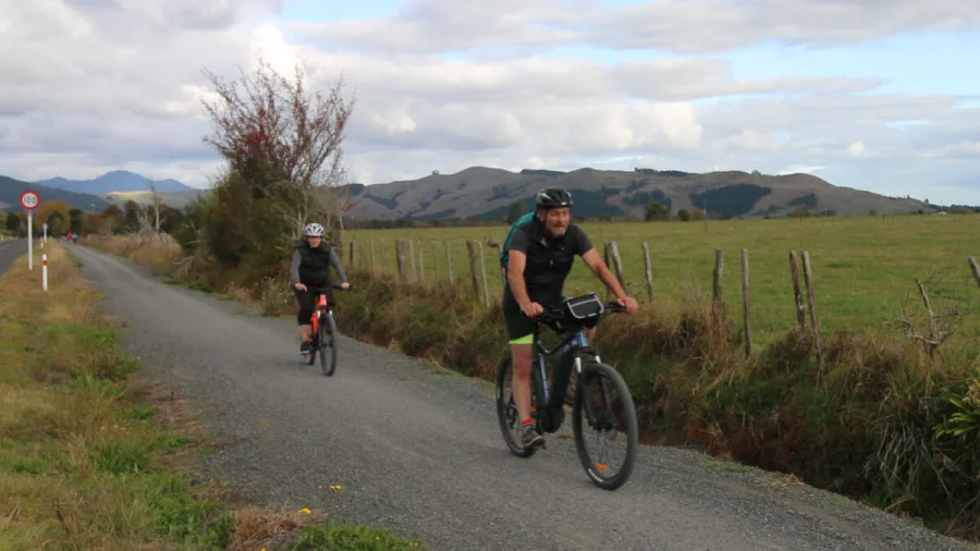 Two e-bike riders cycling along a quiet country road with mountains in the distance