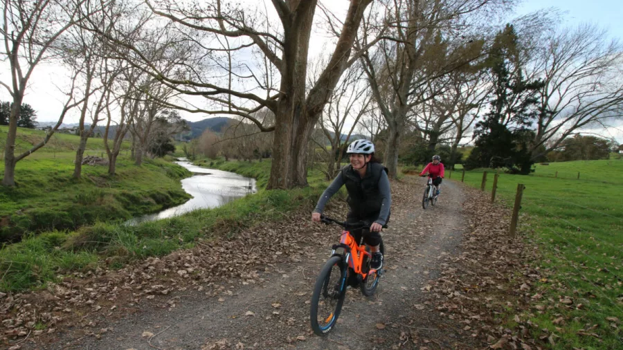 E-bikers on a gravel trail covered in autumn leaves beside a winding river