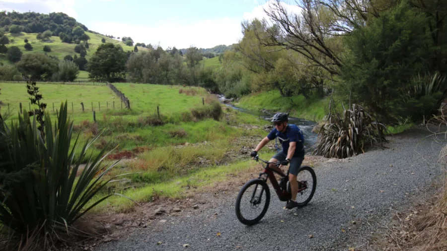 Man riding an e-bike on a gravel track through green pastureland and native bush