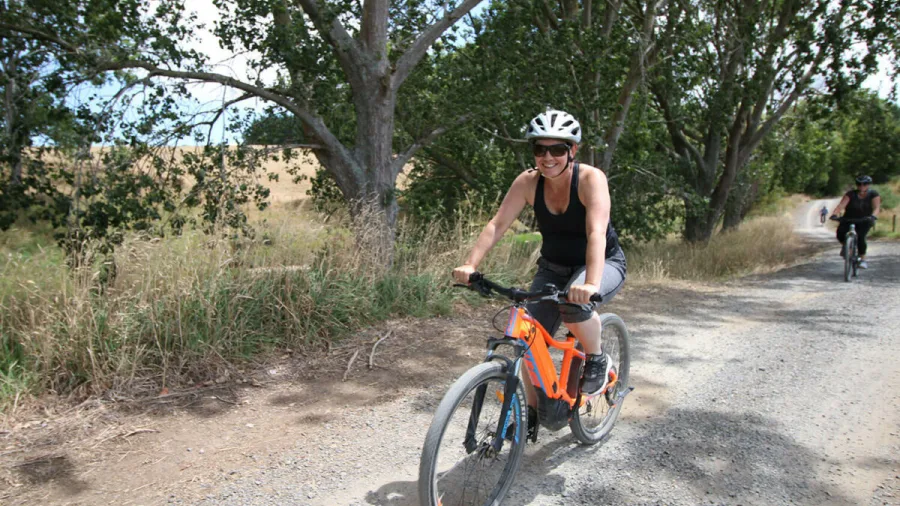Woman riding an orange e-bike on a gravel path through Karangahake Gorge