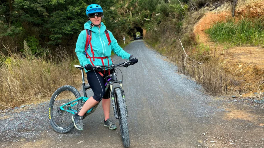 Female cyclist smiling at the entrance of a forest tunnel on the Twin Coast Cycle Trail