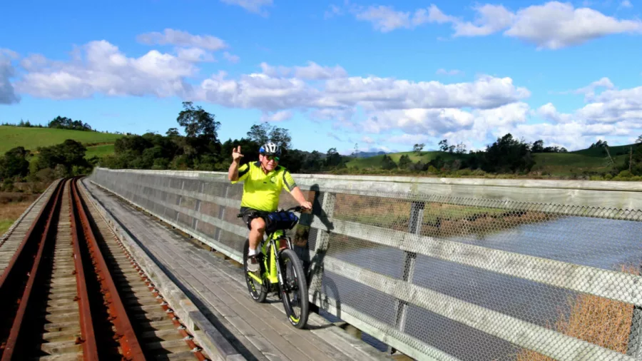 Cyclist giving a shaka sign while riding across a wooden bridge next to train tracks