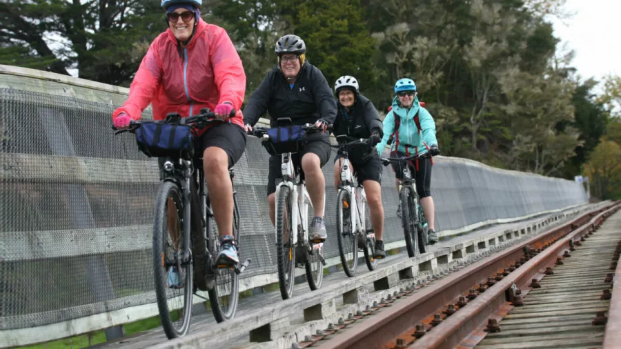 Group of women cyclists riding closely together on a rail bridge section of the trail