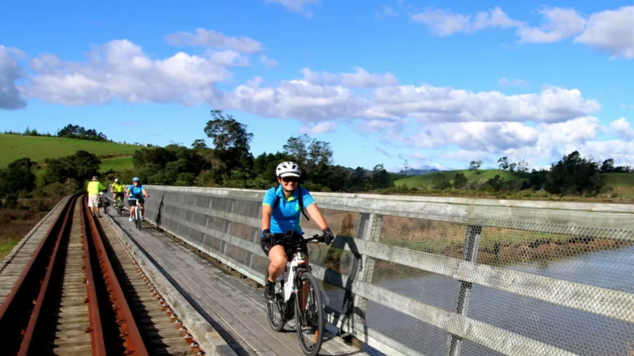 Group of cyclists riding over a bridge next to old railway tracks on the Twin Coast Trail