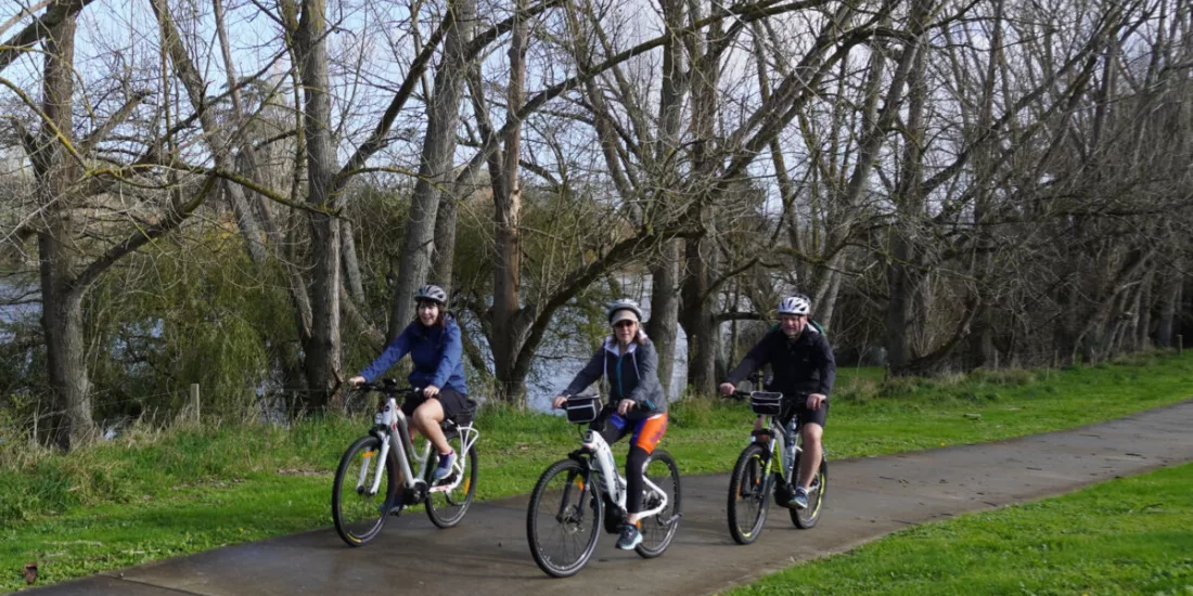 Three cyclists riding past bare winter trees along the Waikato River trail