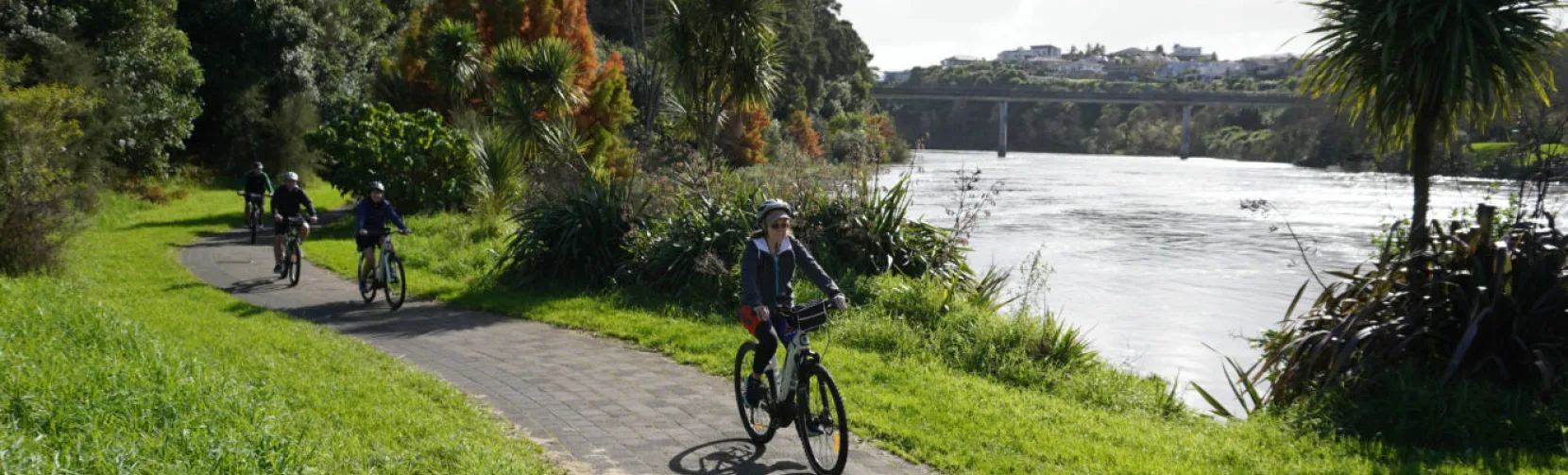 E-bike group tour riding beside the Waikato River with a bridge in the background