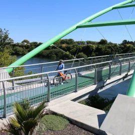 Cyclist riding across modern green bridge on the Waikato River during Te Awa River Ride