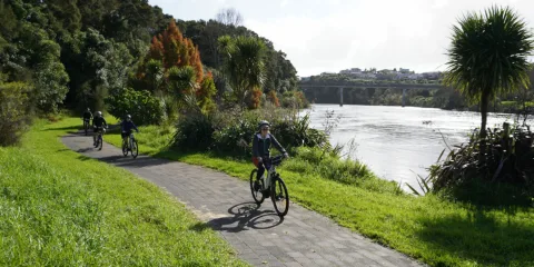 E-bike group tour riding beside the Waikato River with a bridge in the background