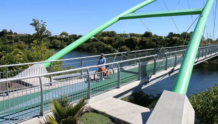Cyclist riding across modern green bridge on the Waikato River during Te Awa River Ride