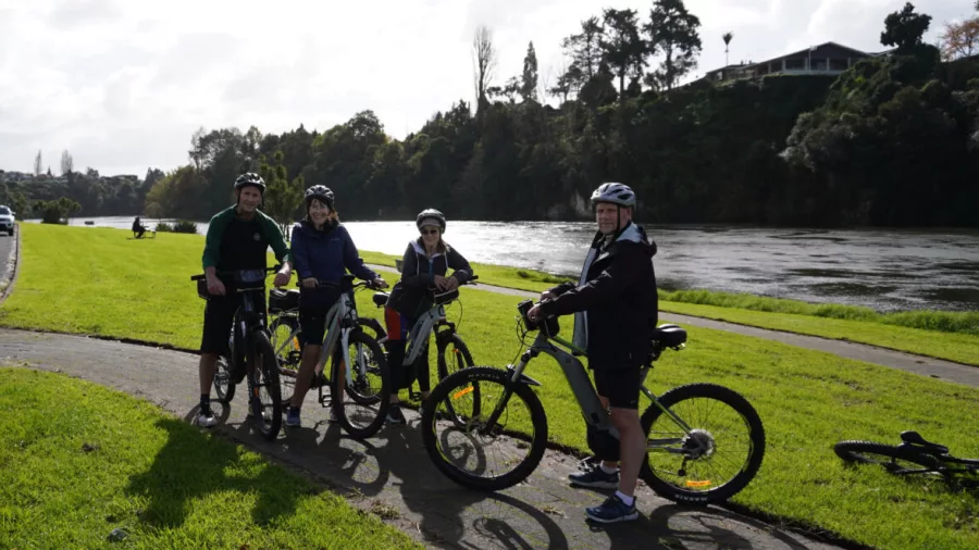 Group of cyclists posing beside the Waikato River during an e-bike tour
