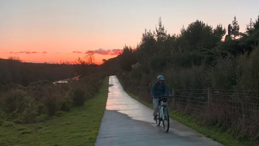 Cyclist riding solo on Te Awa River Ride path during a glowing Waikato sunset