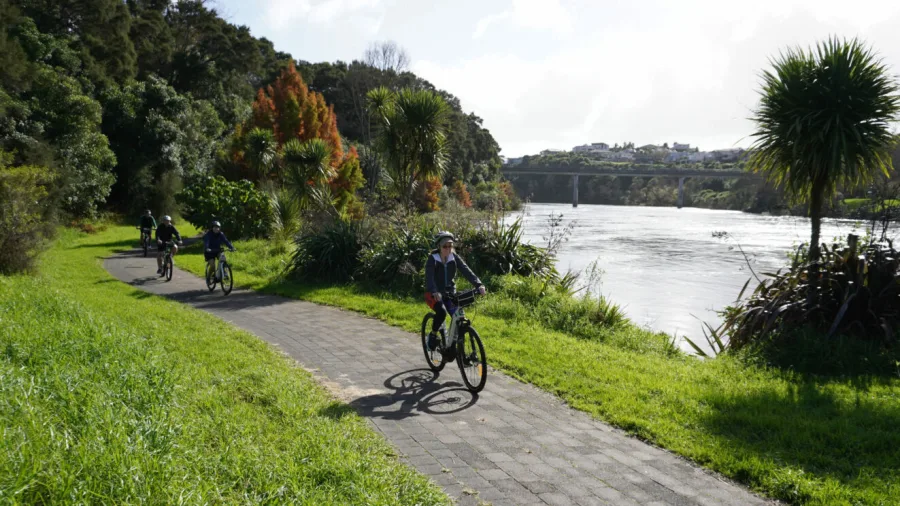 E-bike group tour riding beside the Waikato River with a bridge in the background