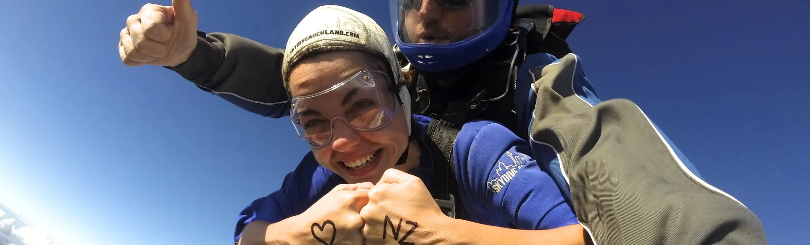 Skydiver with ‘I ❤️ NZ’ written on hands during tandem jump over Auckland