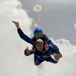 Happy tandem skydivers smiling mid-air surrounded by soft white clouds