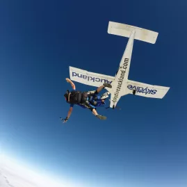 Tandem skydivers exiting plane high above Auckland with clear blue skies