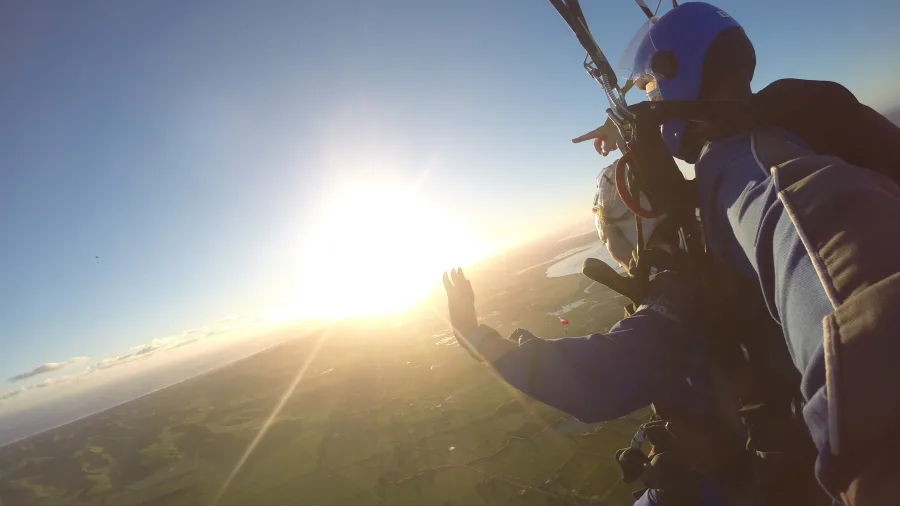 Skydivers gliding under parachute towards sunset-lit farmland near Auckland