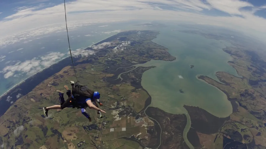 Tandem skydivers descending above winding rivers and estuary on Auckland’s coast