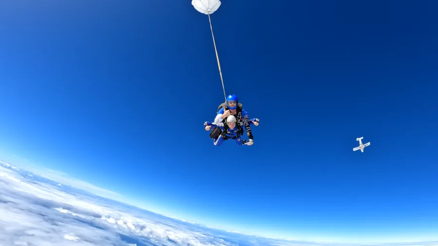 Skydivers descending through vivid blue skies with white clouds below in Auckland