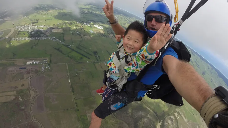 Child and instructor tandem skydiving over scenic Auckland countryside