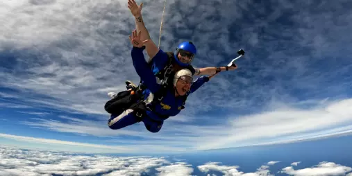 Tandem skydivers freefalling above the clouds with dramatic sky and ocean views near Auckland, New Zealand.