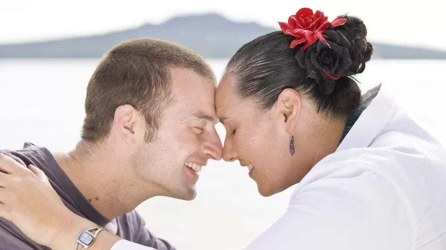 Smiling couple exchanging a hongi with Rangitoto Island in the background